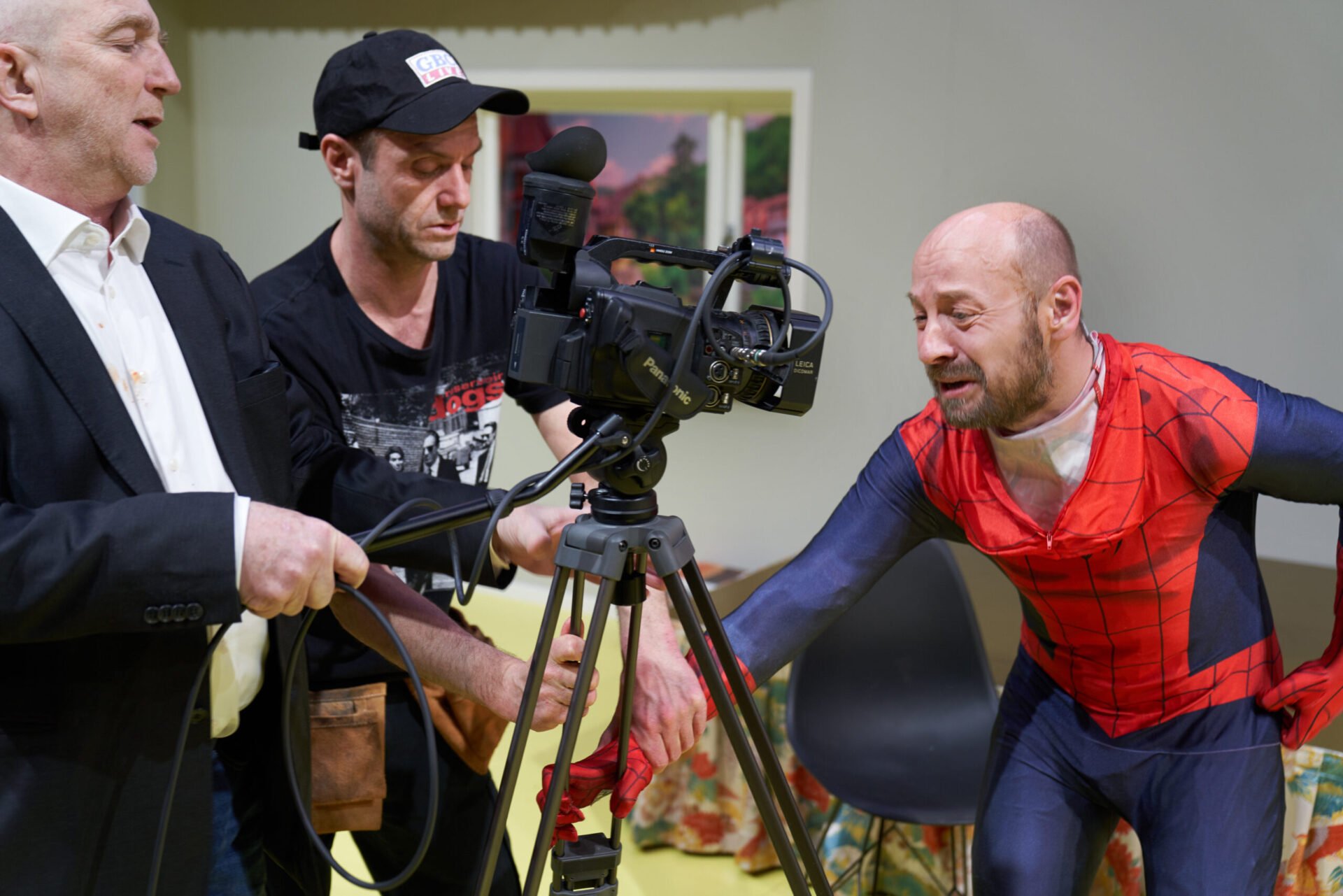 En mann i spidermanndrakt gråter inn i et kamera. To menn filmer.