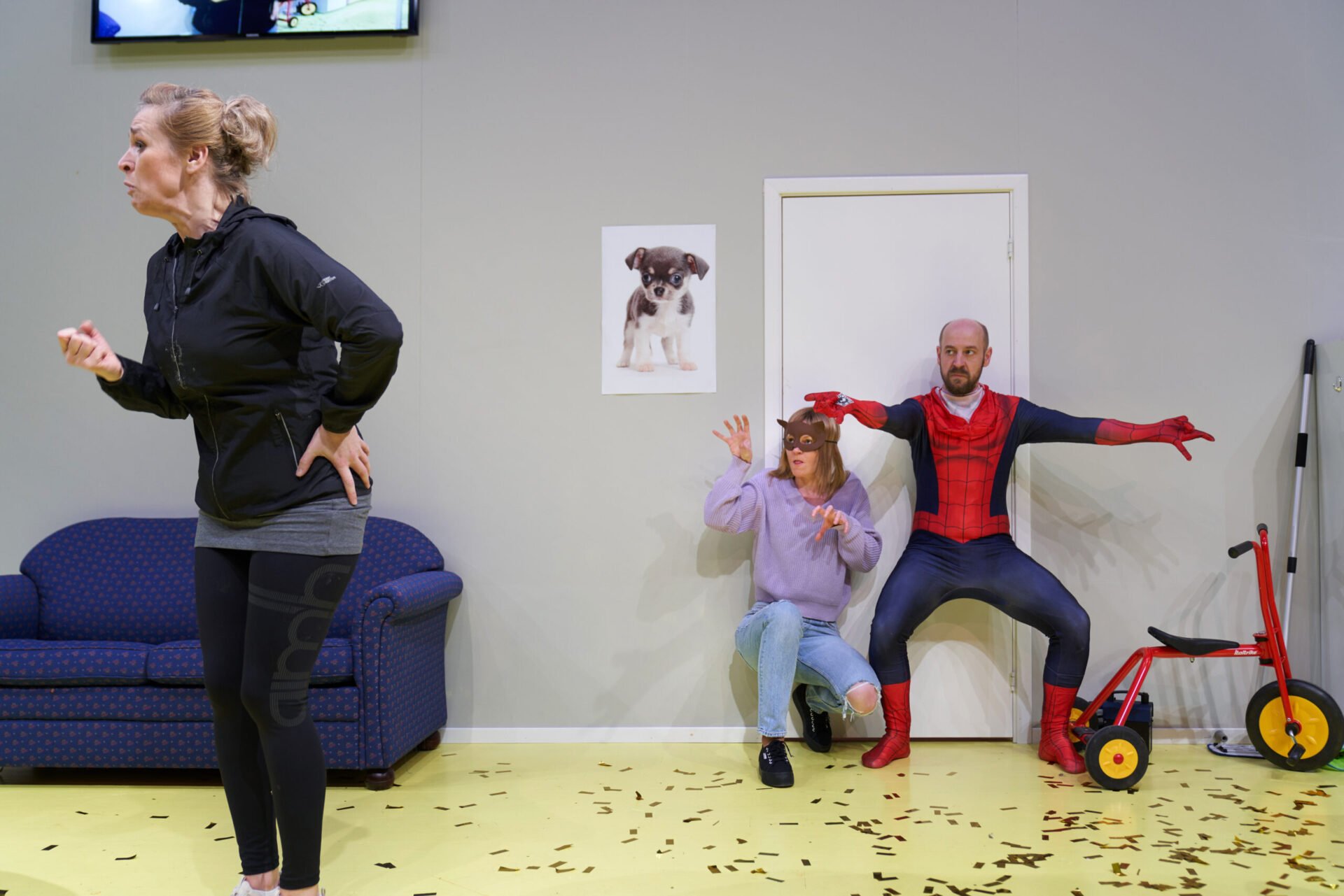 En kvinne står og kjefter på noen mens en mann i spidermanndrakt og en kvinne med kattemaske ser på.