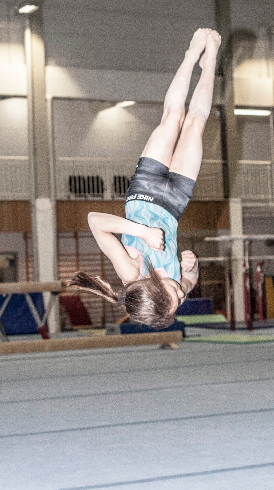 En jente i en turnhall er opp-ned i luften.