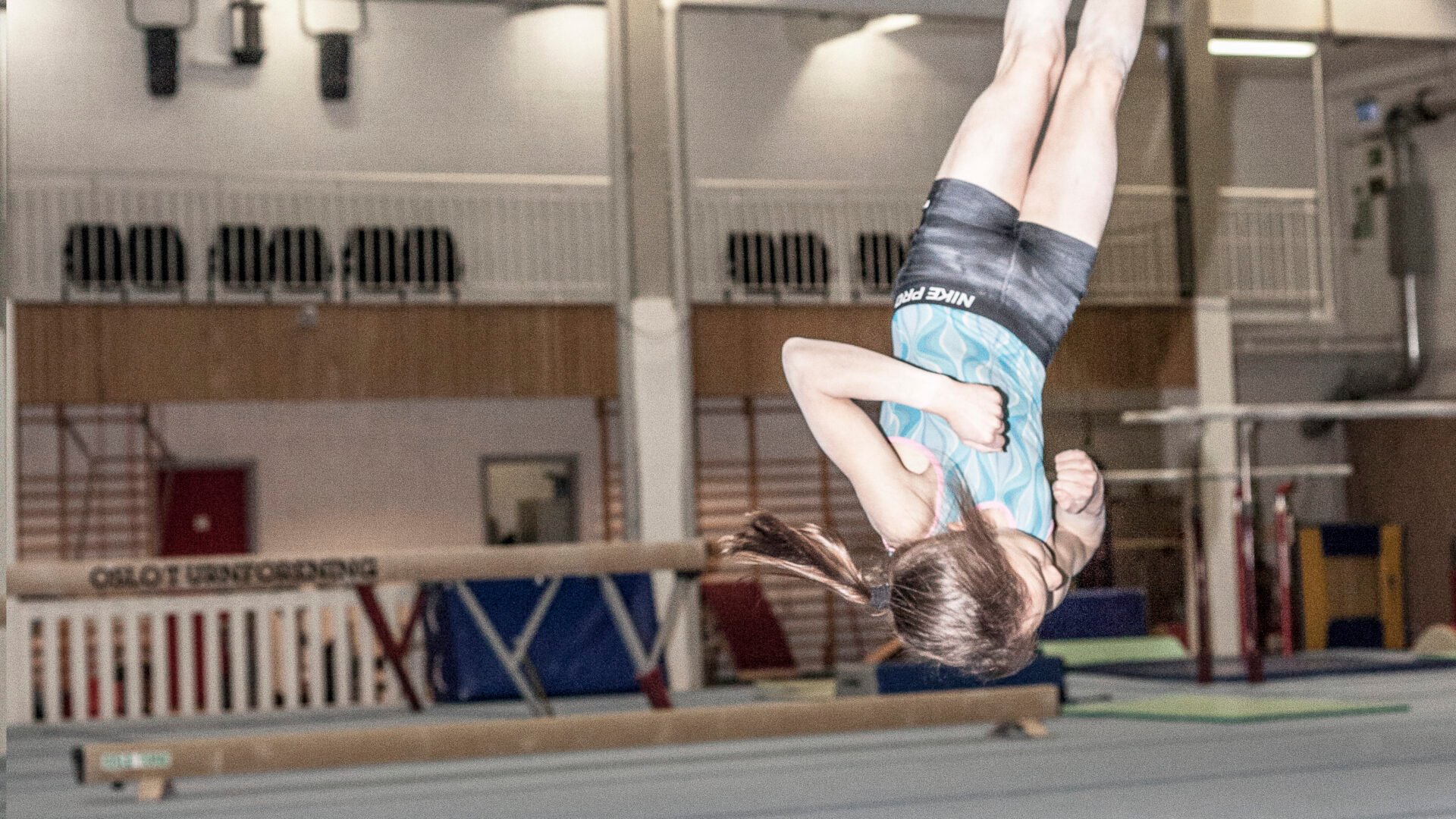 En jente i en turnhall er opp-ned i luften.