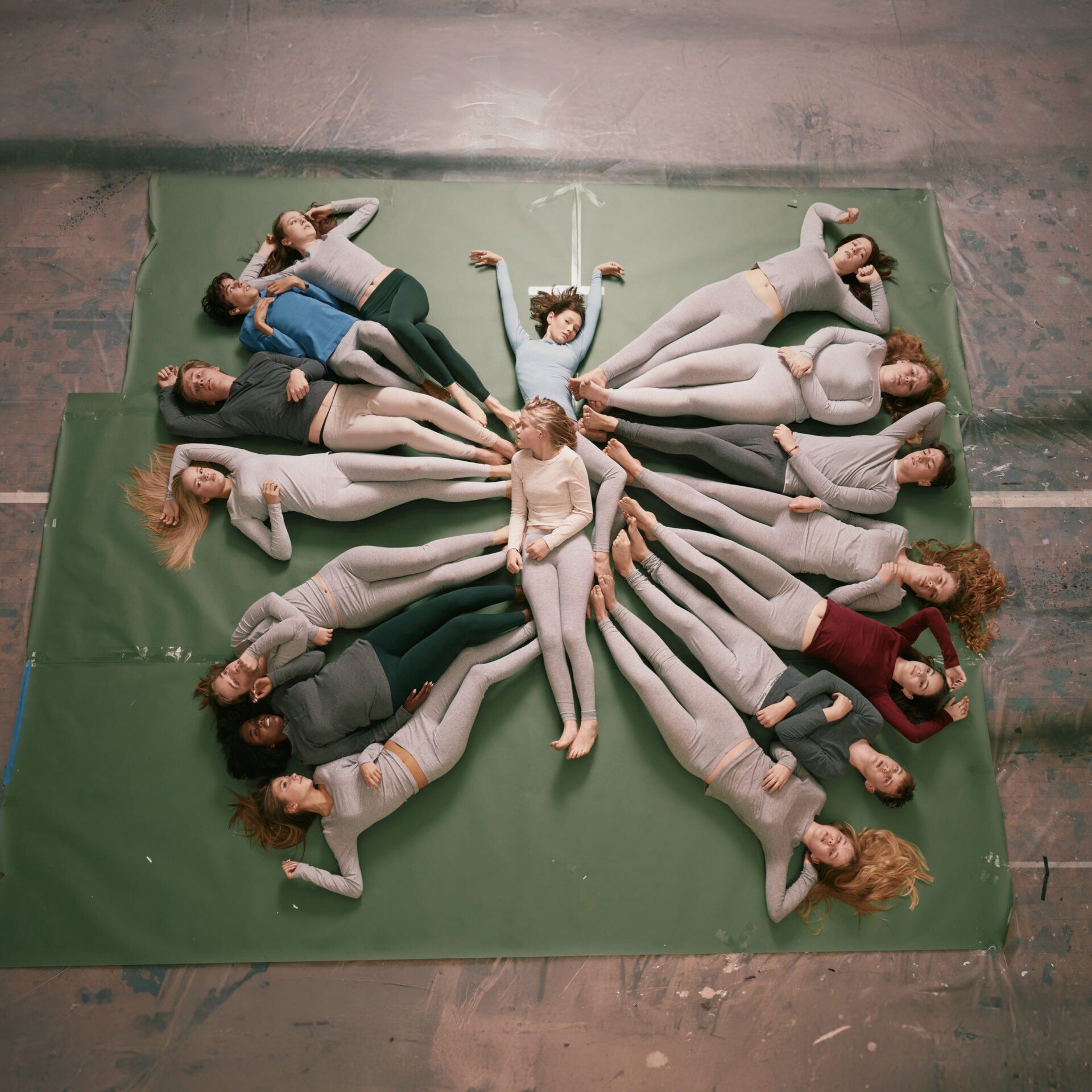 En gruppe ungdommer ligger spredt ut på et gulv og former en sommerfugl.