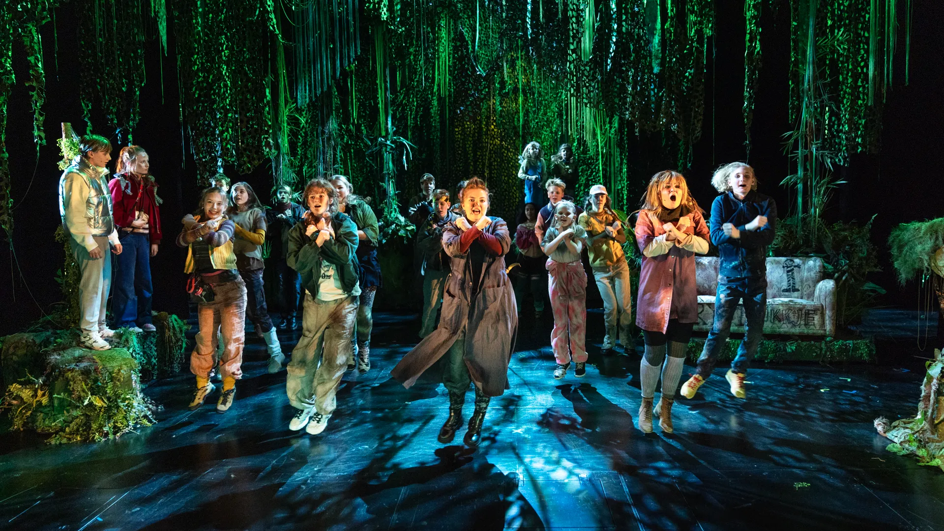 En gruppe unge iført kostyme som danser på en teaterscene. Rundt dem er det lagt til et skoglandskap.
