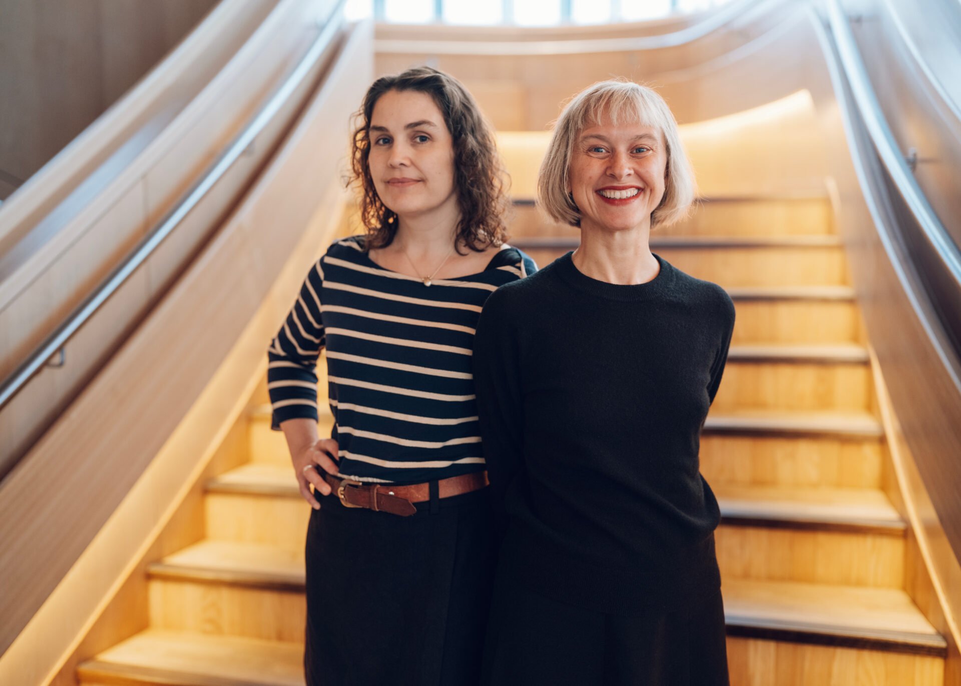To smilende kvinner står foran en lang tretrapp.