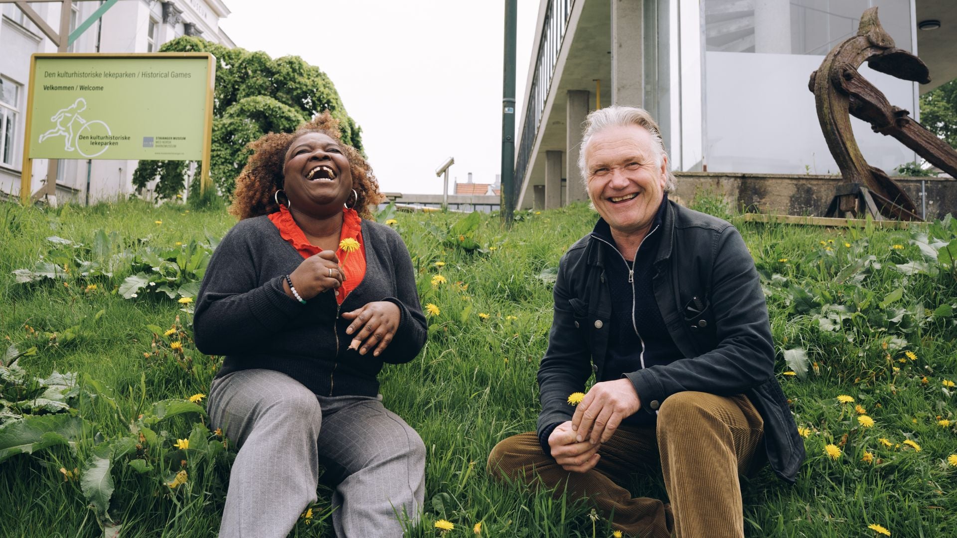 Kim Fairchild og Espen Hana sitter blant løvetenner på en gressplen.