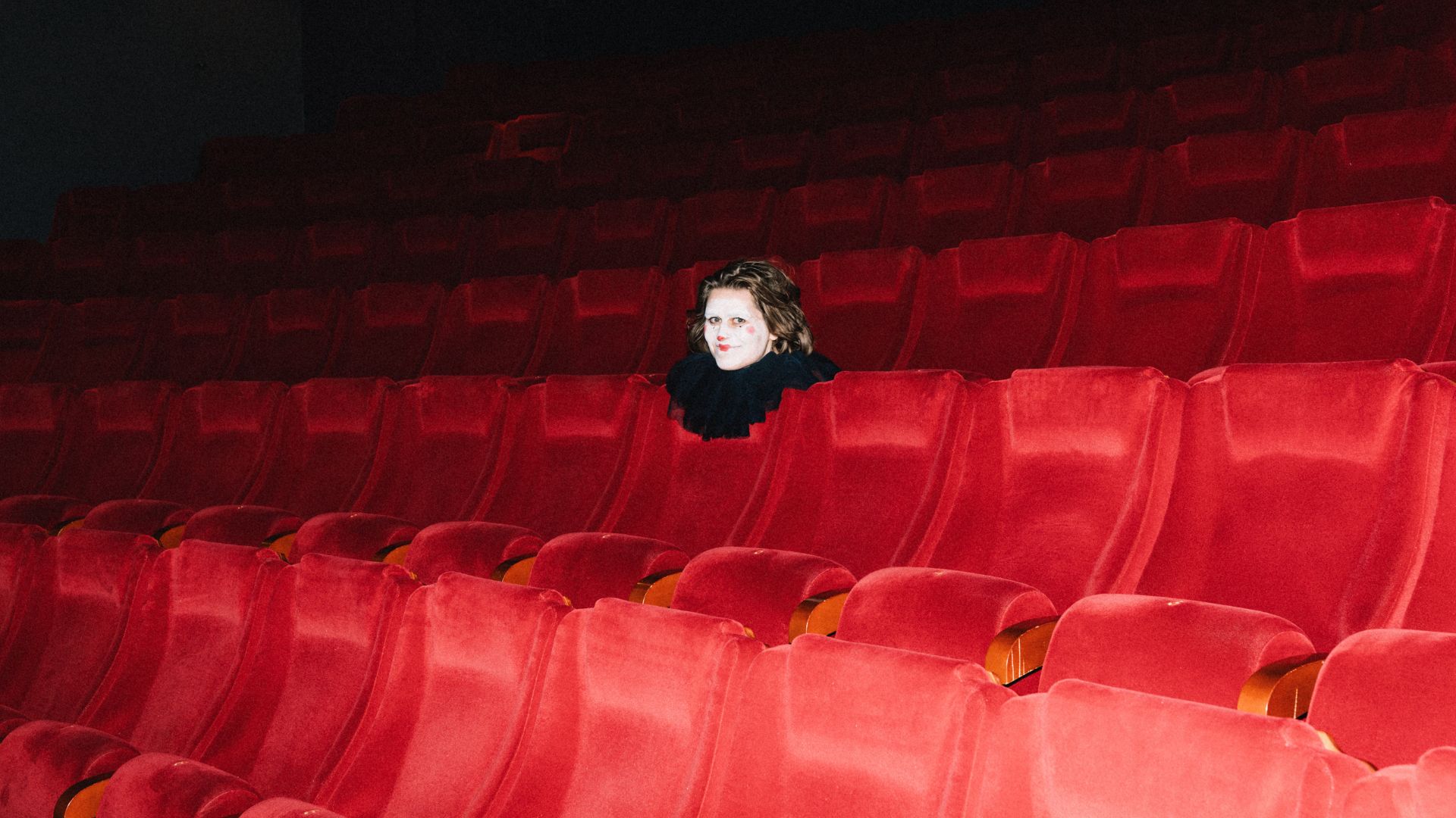 Marie Kallevik i klovnekostyme sitter alene i en sal.